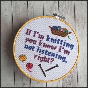 May include: White embroidery hoop with a yellow wooden frame. The embroidery reads "If I'm knitting, you know I'm not listening, right?" with a basket of yarn, two knitting needles, and two balls of yarn.