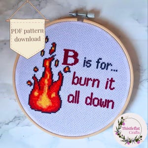 May include: Cross-stitch embroidery in a wooden hoop. The design features a stylized flame in red and orange, with the text "B is for... burn it all down" in red. A banner reads "PDF pattern download".