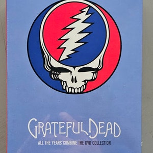 May include: A blue and pink Grateful Dead logo with a skull and lightning bolt design. The text "Grateful Dead" is written in white below the logo. The text "All the Years Combine The DVD Collection" is written in white below the logo.