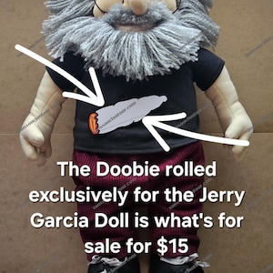 May include: A plush doll resembling a man with a gray beard, glasses, and a black shirt. The shirt features a graphic of a rolled item. The doll's pants are burgundy corduroy, and it wears black shoes. The text on the image says "The Doobie rolled exclusively for the Jerry Garcia Doll is what's for sale".