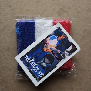 May include: A blue, white, and red wristband with a photo card featuring a person playing a guitar. The card has the text "The Phil Zone" printed on it.