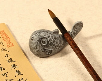 May include: A grey cast iron fish-shaped brush holder with a brown wooden brush resting on top. The brush holder has a textured surface and a large eye.