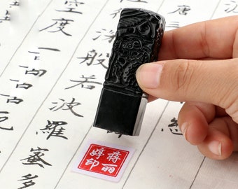 May include: A black carved wooden stamp with a red and white ink pad. The stamp has a detailed design and the ink pad says "印丽".