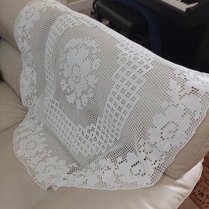 May include: White crocheted doily with a floral pattern, draped over a white sofa.