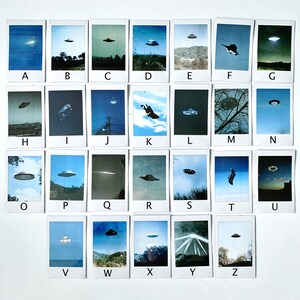 Puede incluir: Un conjunto de 26 fotos de estilo Polaroid, cada una con una letra diferente del alfabeto y una imagen borrosa de un OVNI. Las fotos est&aacute;n ordenadas alfab&eacute;ticamente.