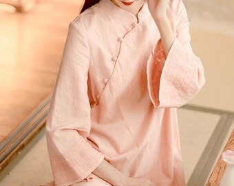 May include: A pale pink, long-sleeved dress with a mandarin collar and button closures. The dress has a relaxed fit and is made of a lightweight fabric.