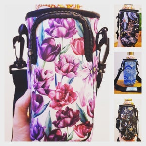 K&ouml;nnte beinhalten: Ein wei&szlig;er Neopren-Flaschenhalter mit einem Blumendruck mit violetten, rosa und gr&uuml;nen Tulpen. Der Halter hat einen schwarzen Rei&szlig;verschluss und einen schwarzen verstellbaren Riemen.