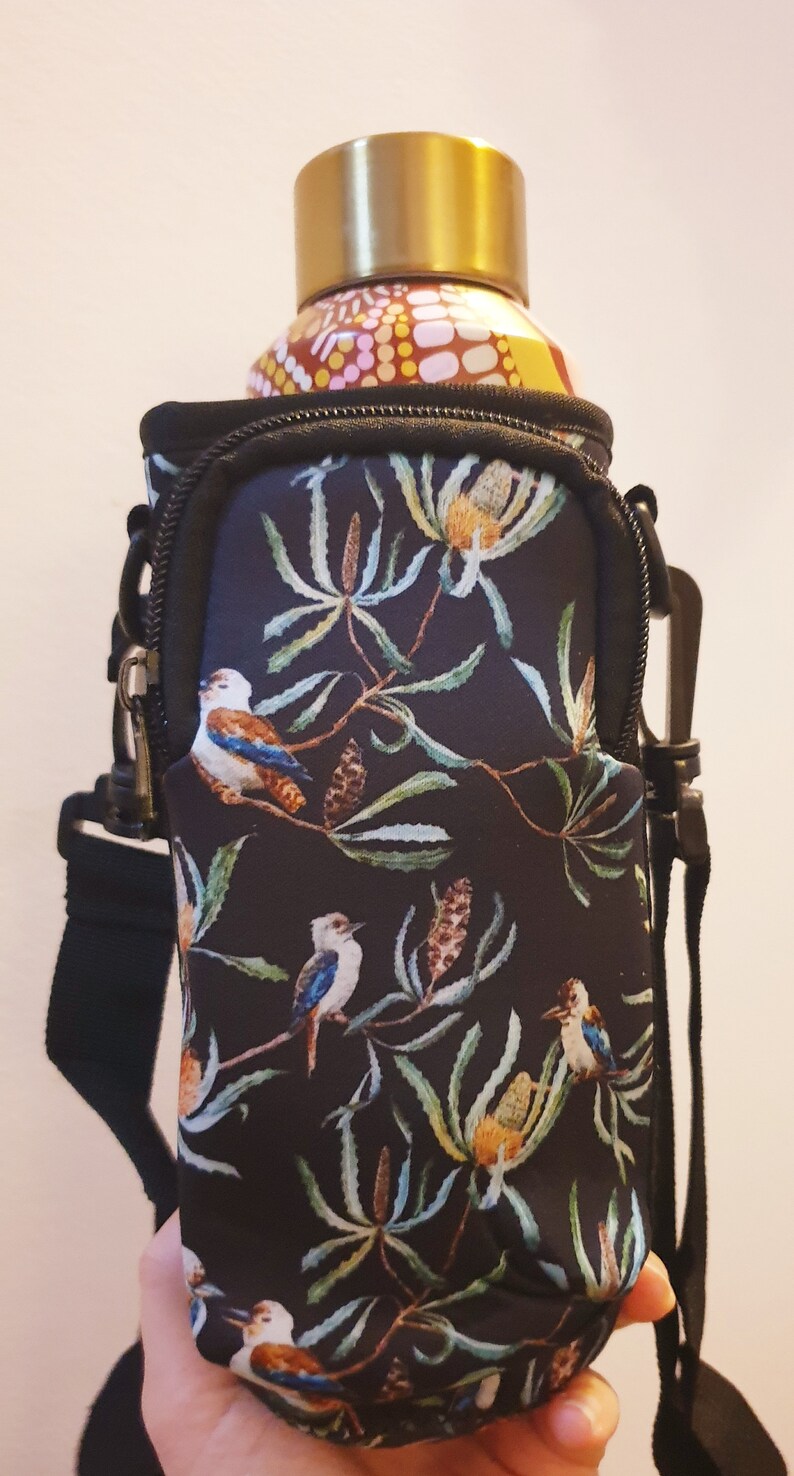 K&ouml;nnte beinhalten: Schwarzer Neopren-Wasserflaschenhalter mit Blumen- und Vogelmotiv. Der Halter hat einen Rei&szlig;verschluss und einen verstellbaren Riemen. Die Flasche ist nicht im Lieferumfang enthalten.