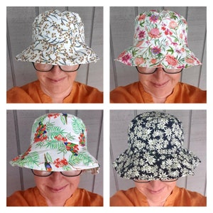 May include: Four different styles of bucket hats with various floral and bird patterns. The hats are white with different coloured patterns. The hats are worn by a person with glasses.
