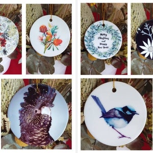 May include: Assortment of round ceramic baubles featuring Australian flora and fauna. Designs include a kookaburra, a wattle, a banksia, a wreath with the text "Merry Christmas and Happy New Year", a koala wearing a Santa hat and glasses, and a blue wren.