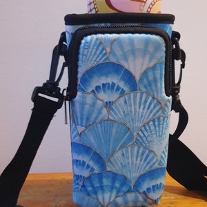 K&ouml;nnte beinhalten: Ein blauer und wei&szlig;er Wasserflaschenhalter mit Rei&szlig;verschlussfach und verstellbarem Riemen. Der Halter hat ein Muster aus blauen und wei&szlig;en Muscheln.