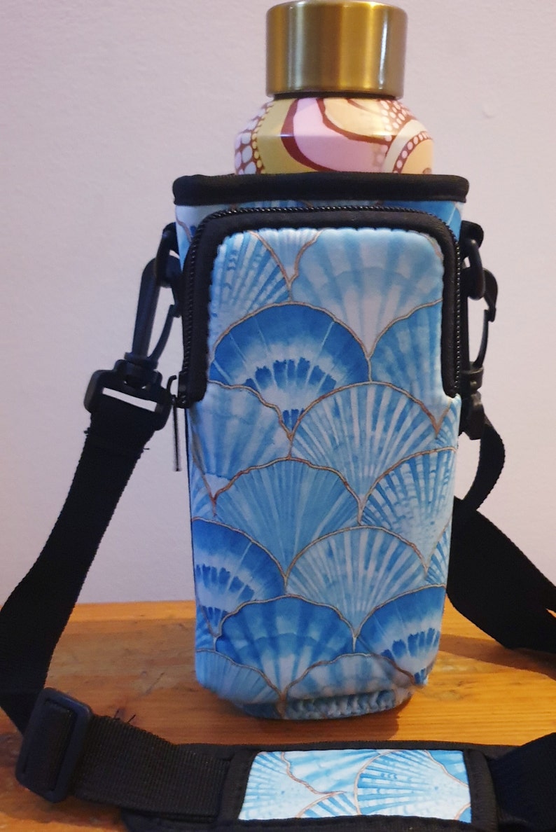 K&ouml;nnte beinhalten: Ein blauer und wei&szlig;er Wasserflaschenhalter mit Rei&szlig;verschlussfach und verstellbarem Riemen. Der Halter hat ein Muster aus blauen und wei&szlig;en Muscheln.