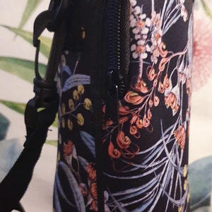 K&ouml;nnte beinhalten: Schwarze isolierte Wasserflaschenh&uuml;lle mit einem Blumendruck mit rosa, blauen und gelben Blumen. Die H&uuml;lle hat einen Rei&szlig;verschluss und einen schwarzen Gurt.