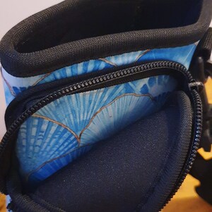 K&ouml;nnte beinhalten: Ein blauer und goldfarbener Neopren-Wasserflaschenhalter mit schwarzem Rei&szlig;verschluss und schwarzem Gurt.