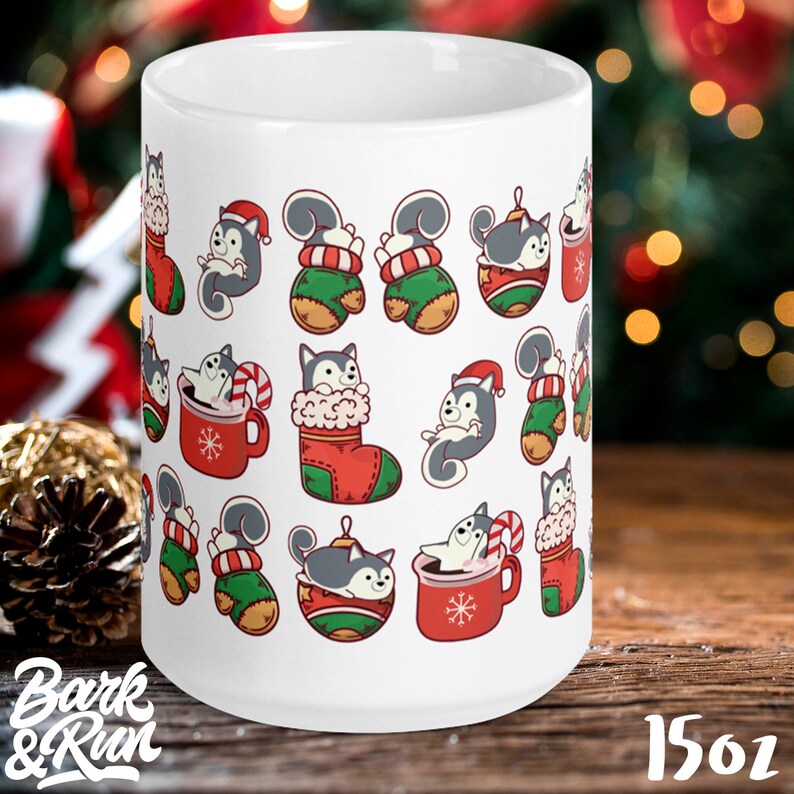May include: White ceramic mug with a Christmas-themed design featuring a pattern of grey and white husky dogs wearing Santa hats, holding candy canes, and sitting in Christmas stockings, ornaments, and mugs. The mug is 15 oz.