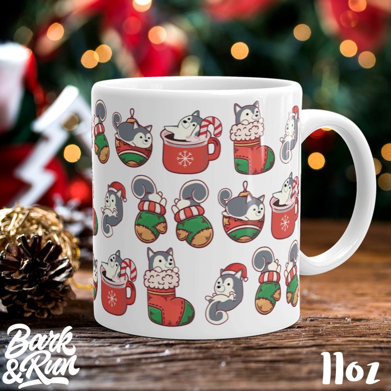May include: White ceramic mug with a Christmas-themed design featuring a pattern of cartoon huskies in various holiday settings, including a stocking, a mug of hot chocolate, and a Christmas ornament. The mug is 11 oz.