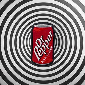 Pode incluir: Um patch vermelho em forma de lata de Dr. Pepper com letras brancas e o texto "BAAAABY". O patch está centrado em um fundo espiral em preto e branco.