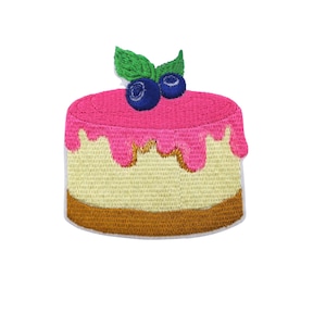 Peut inclure: Un patch brodé en forme de gâteau rose et jaune avec des myrtilles bleues et des feuilles vertes sur le dessus.