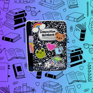 May include: A black composition notebook with a white border and the words "Composition Notebook" printed on the front. The notebook has various colorful stickers on it, including a rainbow, a frog, a heart, a cup of tea, a flower, and a bear.