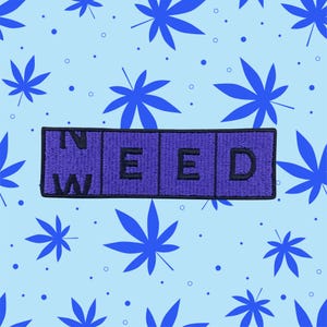 May include: Purple embroidered patch with the word "IN WEED" in black letters.