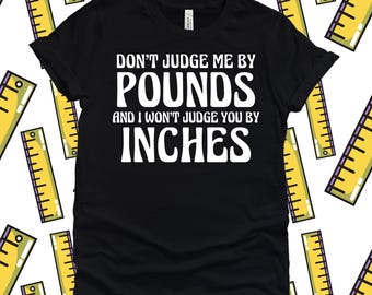 Könnte beinhalten: Schwarzes T-Shirt mit weißem Text: "DON'T JUDGE ME BY POUNDS AND I WON'T JUDGE YOU BY INCHES." Das Shirt ist von einem Muster aus gelben Linealen umgeben. Das Shirt ist aus einem weichen Material.