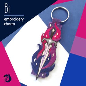 May include: An embroidered charm featuring a sword design in purple, pink, and blue, attached to a purple fabric loop and a silver keyring. The charm has the text "Bi embroidery charm" in white.