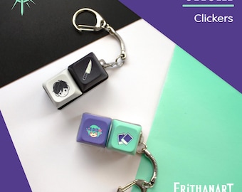 Op de afbeelding: Twee mechanische toetsenbord keycap sleutelhangers. Eén heeft een witte keycap met een zwart karaktergezicht en een zwarte keycap met een mesicoon. De andere heeft een paarse keycap met een bloemengezicht en een mintgroene keycap met twee foto's.
