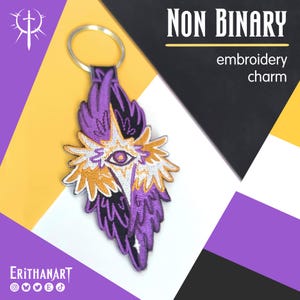 May include: An embroidered keychain charm featuring a central eye motif surrounded by stylized wings in purple, yellow, white, and black thread. The design includes a metal keyring at the top. Text on the image reads "NON BINARY embroidery charm" and "ERITHANART".