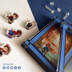 Puede incluir: Una colecci&oacute;n de peque&ntilde;os pines acr&iacute;licos con varias figuras, incluyendo una colocada dentro de un marco rectangular azul con un interior impreso. El texto ErithanArt es visible en la esquina con iconos sociales.