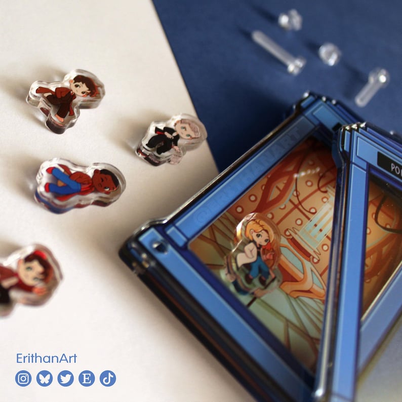 Puede incluir: Una colecci&oacute;n de peque&ntilde;os pines acr&iacute;licos con varias figuras, incluyendo una colocada dentro de un marco rectangular azul con un interior impreso. El texto ErithanArt es visible en la esquina con iconos sociales.