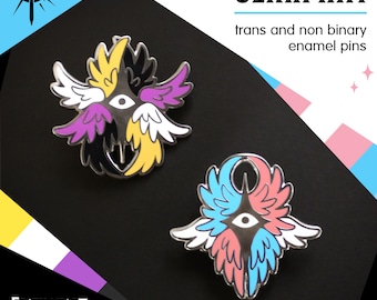 以下が含まれることがあります： SERAPHIM trans and non binary enamel pinsと書かれた2つのエナメルピン。1つは黄色、黒、紫、白の翼と中央の目。もう1つは青、ピンク、白の翼と中央の目がデザインされています。