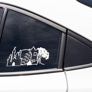 May include: White vinyl decal of a castle, a sphere with squares, and a tree on a black car window.