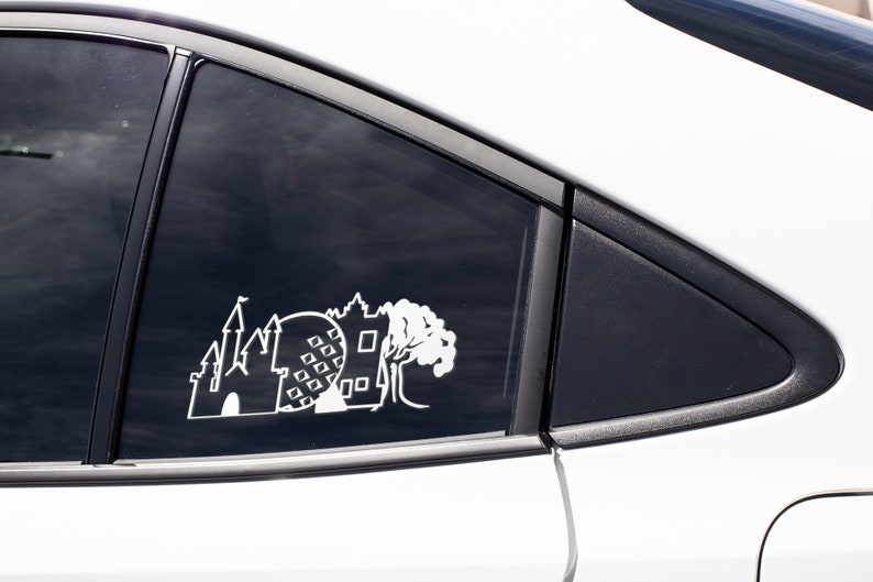 May include: White vinyl decal of a castle, a sphere with squares, and a tree on a black car window.