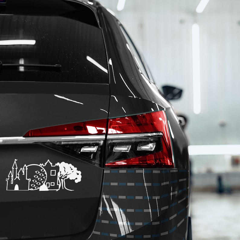May include: Black car with a white sticker of a castle, a sphere, and a tree. The car has a red taillight and a gray and blue patterned design on the back.
