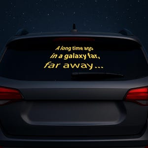 Puede incluir: Calcomanía amarilla en la ventana trasera de un coche. El texto "Hace mucho tiempo, en una galaxia muy, muy lejana..." se muestra en una fuente estilizada, sobre un fondo oscuro con un cielo estrellado.