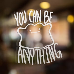 May include: A white vinyl decal featuring a line-art illustration of a blob-shaped creature with two small dots for eyes and a simple curved line for a mouth, accompanied by the text YOU CAN BE ANYTHING in a bold, sans-serif font.
