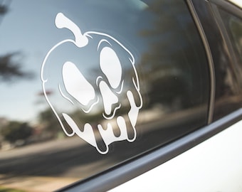 May include: A white vinyl sticker of a melting apple with a skull face. The sticker is on a car window.