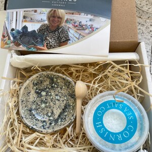 May include: A gift box with a speckled ceramic dish, a small wooden spoon, and a container of Cornish Sea Salt. The box also includes a card with the text "TREGIRLS POTTERY CORNWALL". The dish has a blue and white speckled pattern.