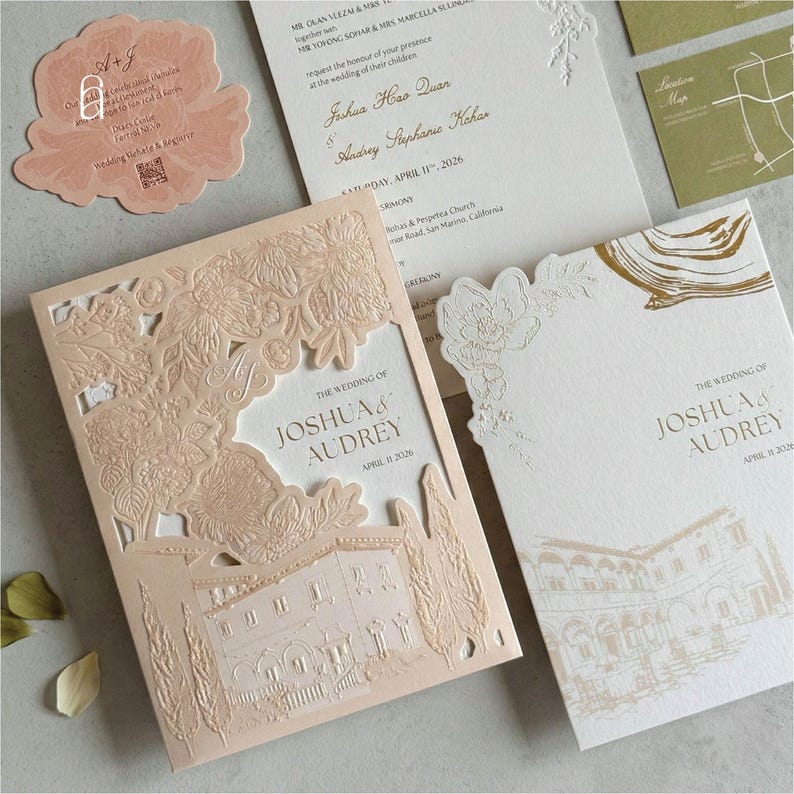 May include: Elegant wedding invitation suite in soft peach and white. The suite includes a laser-cut invitation with a detailed architectural design, RSVP card, and a location map. The text reads "The Wedding of Joshua & Audrey, April 11, 2026."
