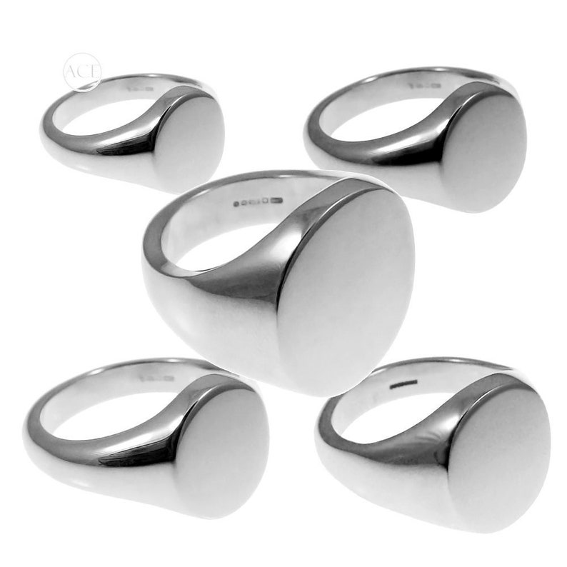 May include: Four silver signet rings with a smooth, oval-shaped top. The rings are stacked on top of each other.