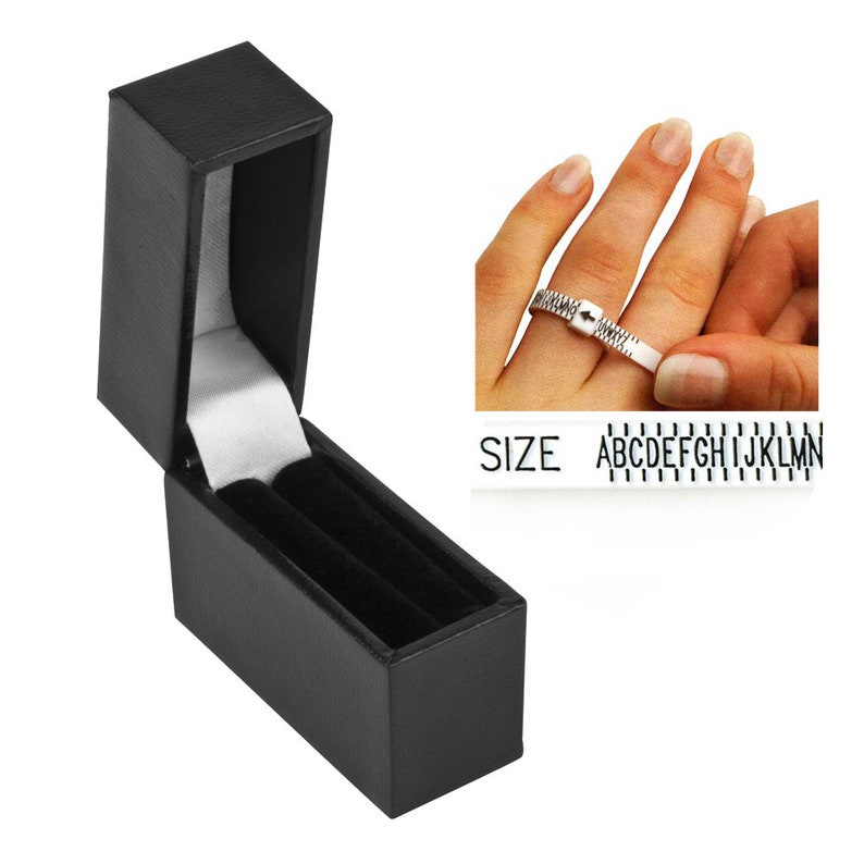May include: Black ring box with a velvet interior. A ring sizer with the letters A through N is shown in the background.