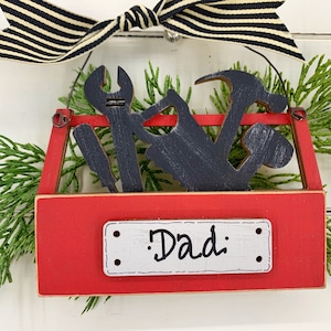 May include: Red wooden toolbox ornament with black silhouette tools and a white label that says "Dad".