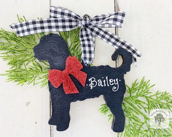 May include: Black wooden dog ornament with a red glitter bow and the name "Bailey" written on it. The ornament is hanging from a black and white checkered ribbon.