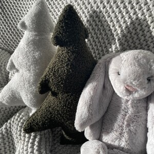 May include: Three plush toys: a white tree, a dark green tree, and a gray bunny. The toys are made of soft, textured material and are arranged on a gray, knitted blanket. The bunny has long, floppy ears and a pink nose.