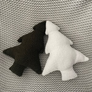 May include: Two tree-shaped decorative pillows. One is dark brown, the other is white. Both pillows have a soft, textured, plush appearance. The pillows are lying on a gray, textured surface.