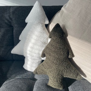 May include: Two tree-shaped decorative pillows. One is white, the other is olive green. Both pillows have a textured, plush appearance. They are resting on a dark gray upholstered surface, with a light-colored pillow in the background.