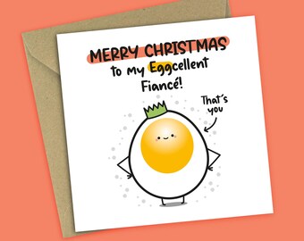 May include: A white greeting card with a cartoon egg character wearing a green crown. The card reads "MERRY CHRISTMAS to my Eggcellent Fiance!" with the text "That's you" and an arrow pointing to the egg.