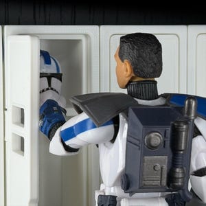 May include: A figure in a white and blue uniform with a black backpack and a helmet. The figure is opening a white cabinet to reveal a matching helmet. The scene is set against a black background.
