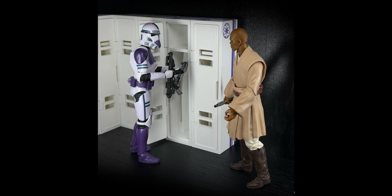 May include: Two action figures from the Star Wars franchise. One figure is a white and purple Stormtrooper, the other is a Jedi in a tan robe. The Stormtrooper is holding a weapon near a white locker.