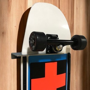 May include: A white skateboard with black wheels and a red cross graphic on the tail. The skateboard is mounted on a wall with a metal bracket.